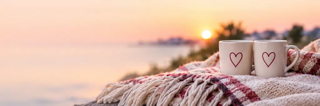 Two heart-patterned mugs on a blanket at sunset